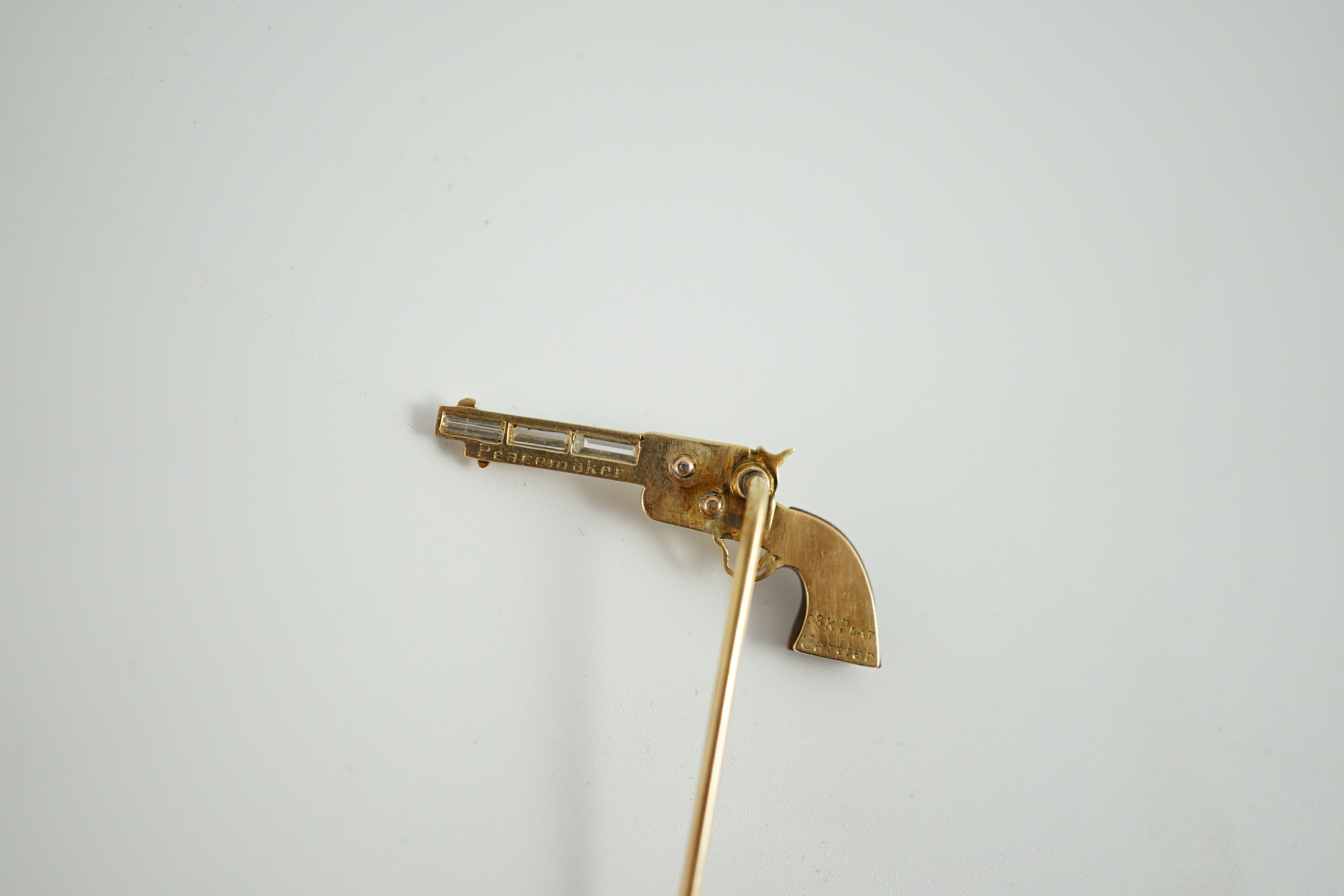 A Cartier 18k gold, platinum and six stone baguette cut diamond set novelty stick pin, modelled and a pistol inscribed 'Peacemaker'
